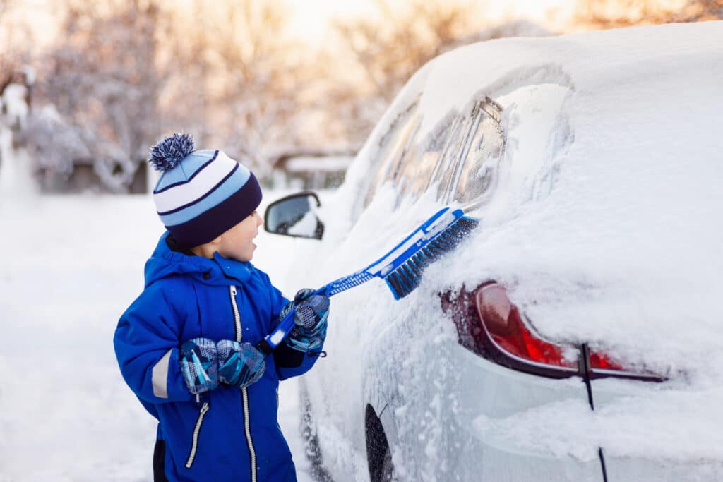 child boy helping to cleaning snow from fathers car