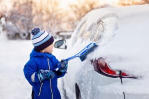 child boy helping to cleaning snow from fathers car