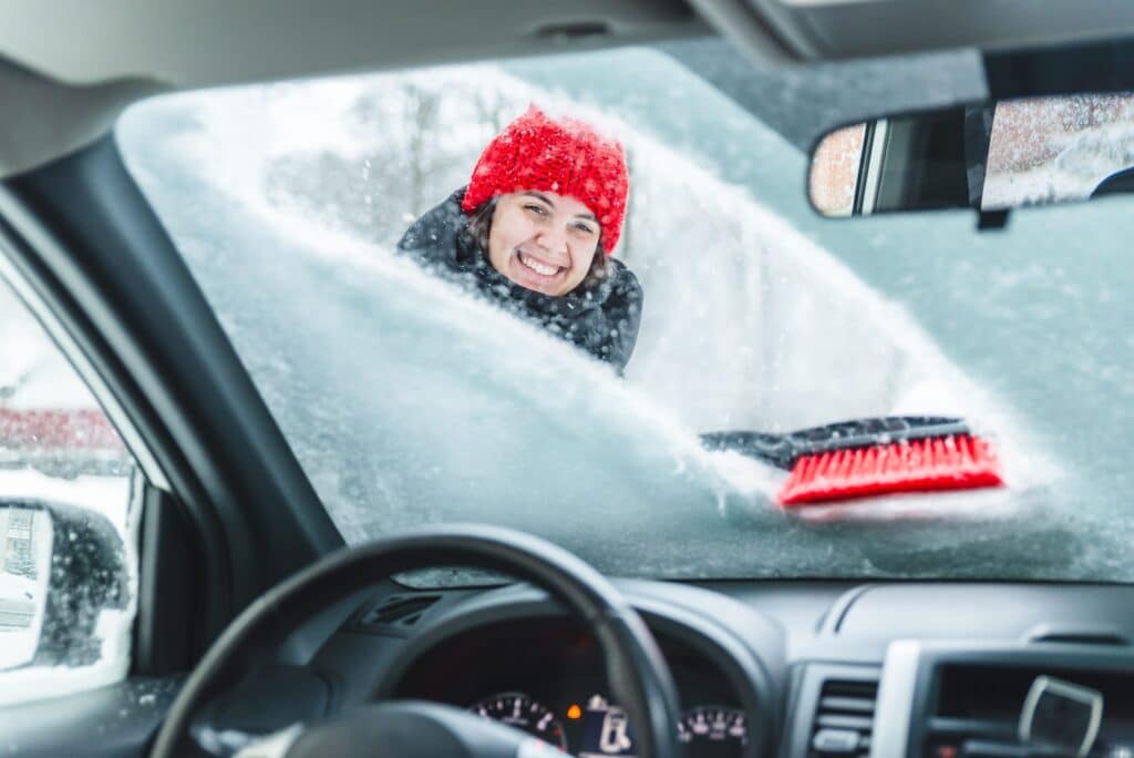 young pretty woman cleaning car after snow storm