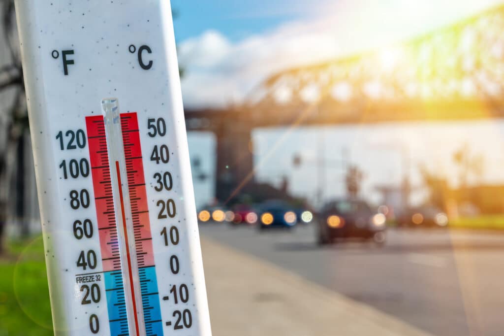 Thermometer in front of cars and traffic during heatwave.